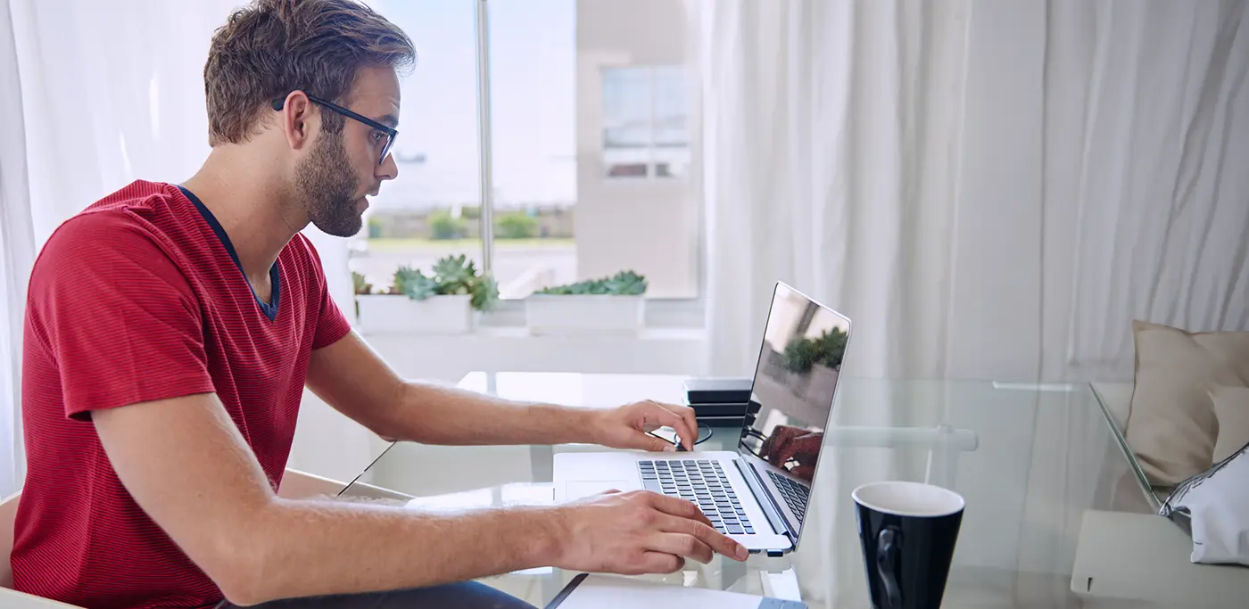 White man working on his laptop at a glass table wearing a red polo shirt