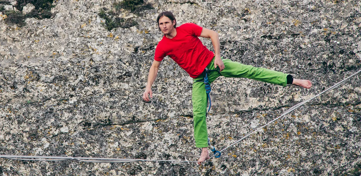 Man in red tshirt crossing a tightrope high up in a mountain gorge