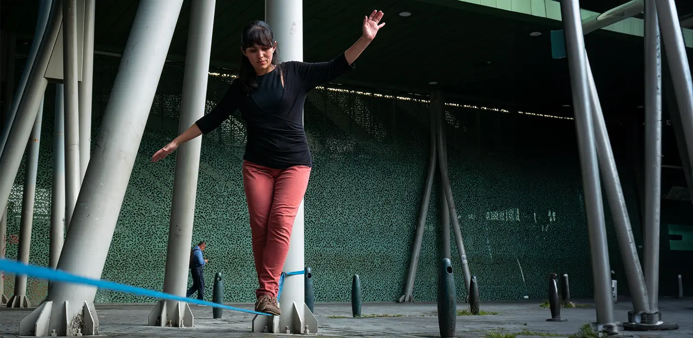 Women in red pants walking across a blue tightrope close to the ground