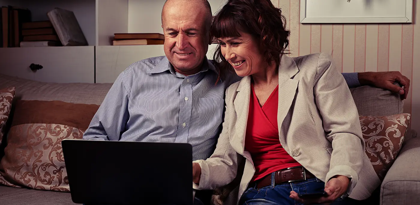 Older couple browsing their laptop, sat together on the sofa