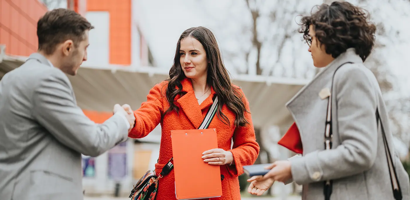 Women in red shaking hands with man in grey coat