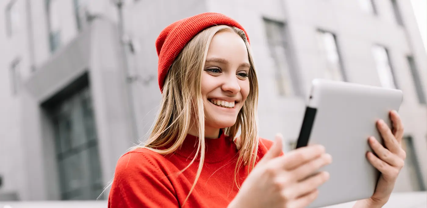 Happy women wearing a red beanie reading an ipad