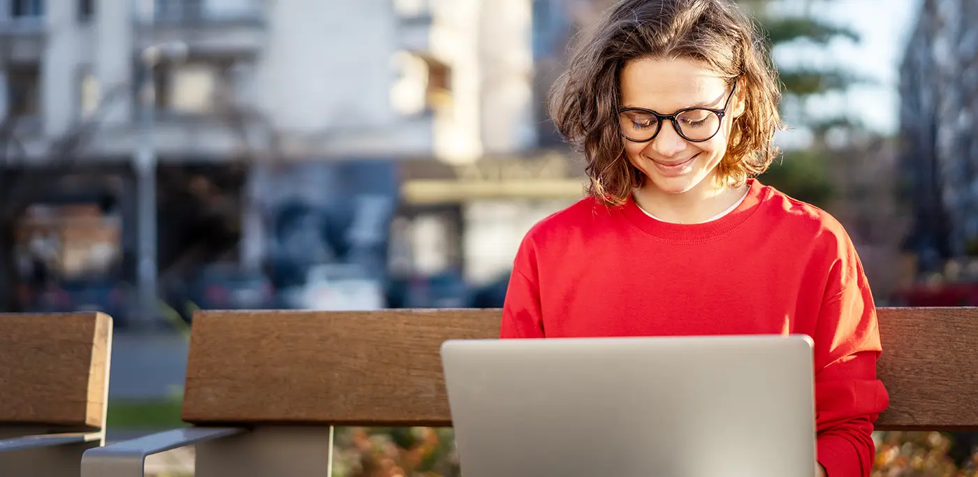 Happy student looking at laptop on park bench