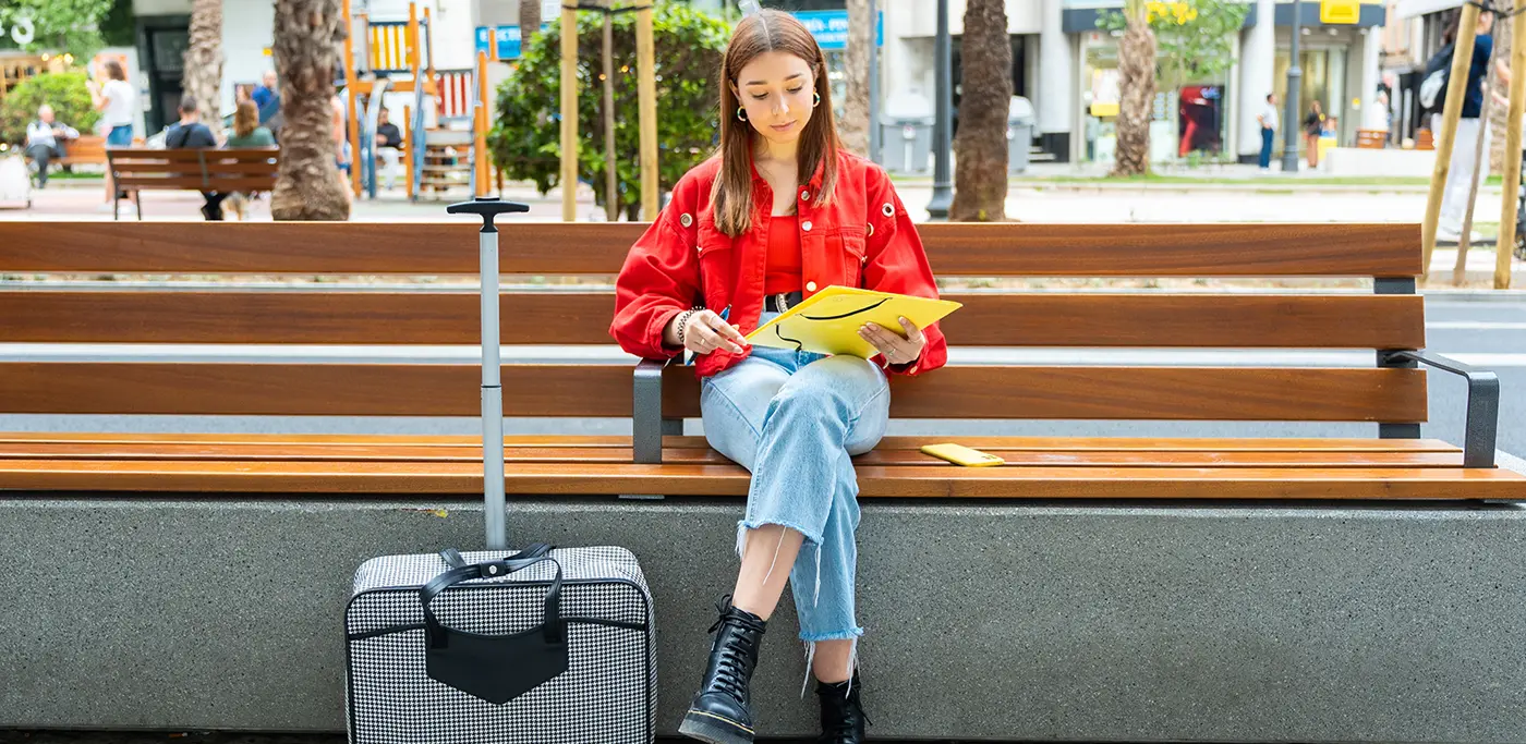 Female student in red hoodie sitting on bench waiting for the bus