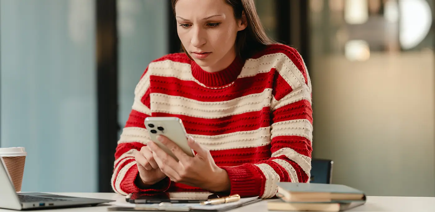 Female student in red jumper looking nervous at phone