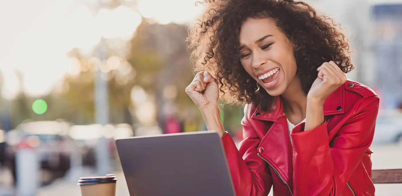 Happy women cheering whilst sat looking at her laptop