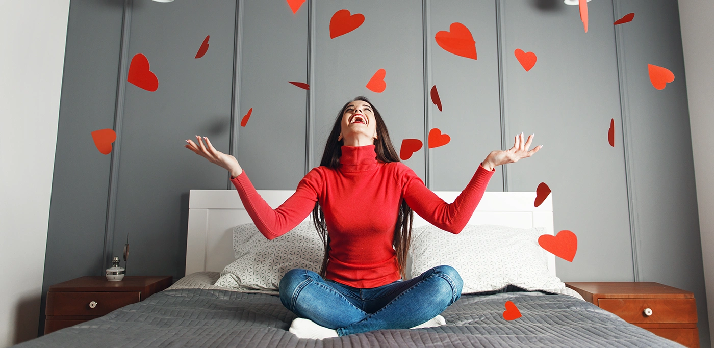 Women in red on bed with latop with falling paper hearts around her